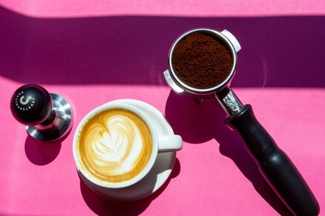 Top down photo of a Counter Culture Coffee tamper, a cappuccino, and a filled portafilter. 