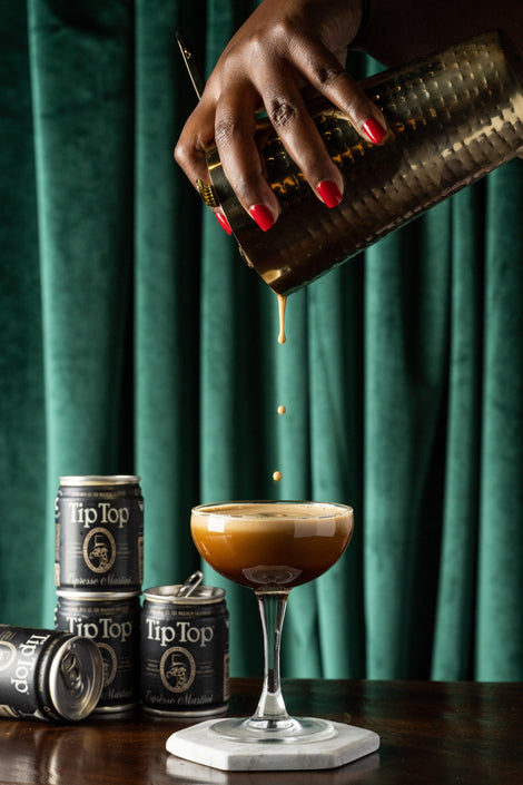 Photo of a hand pouring an espresso martini into a glass from a cocktail shaker.