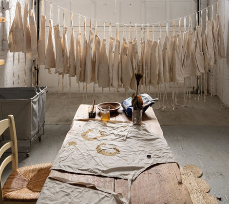 Aprons hang on a line over a table of dye materials in an industrial space.