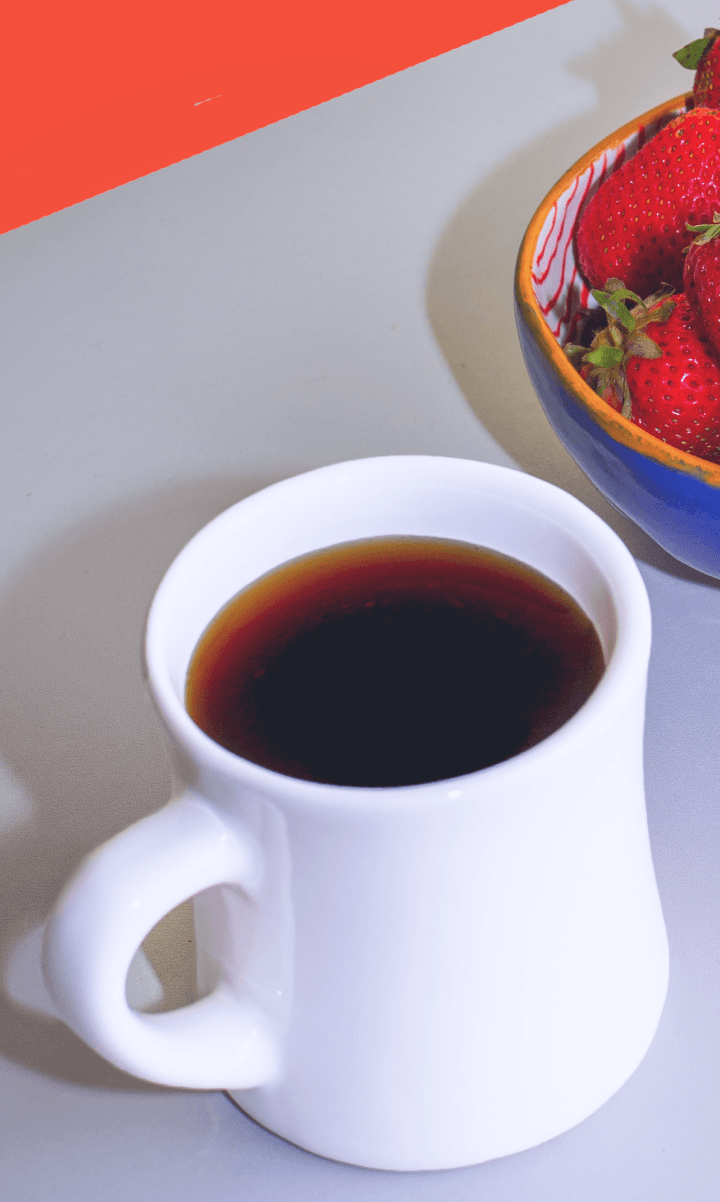 Mug of black coffee next to a bowl of strawberries